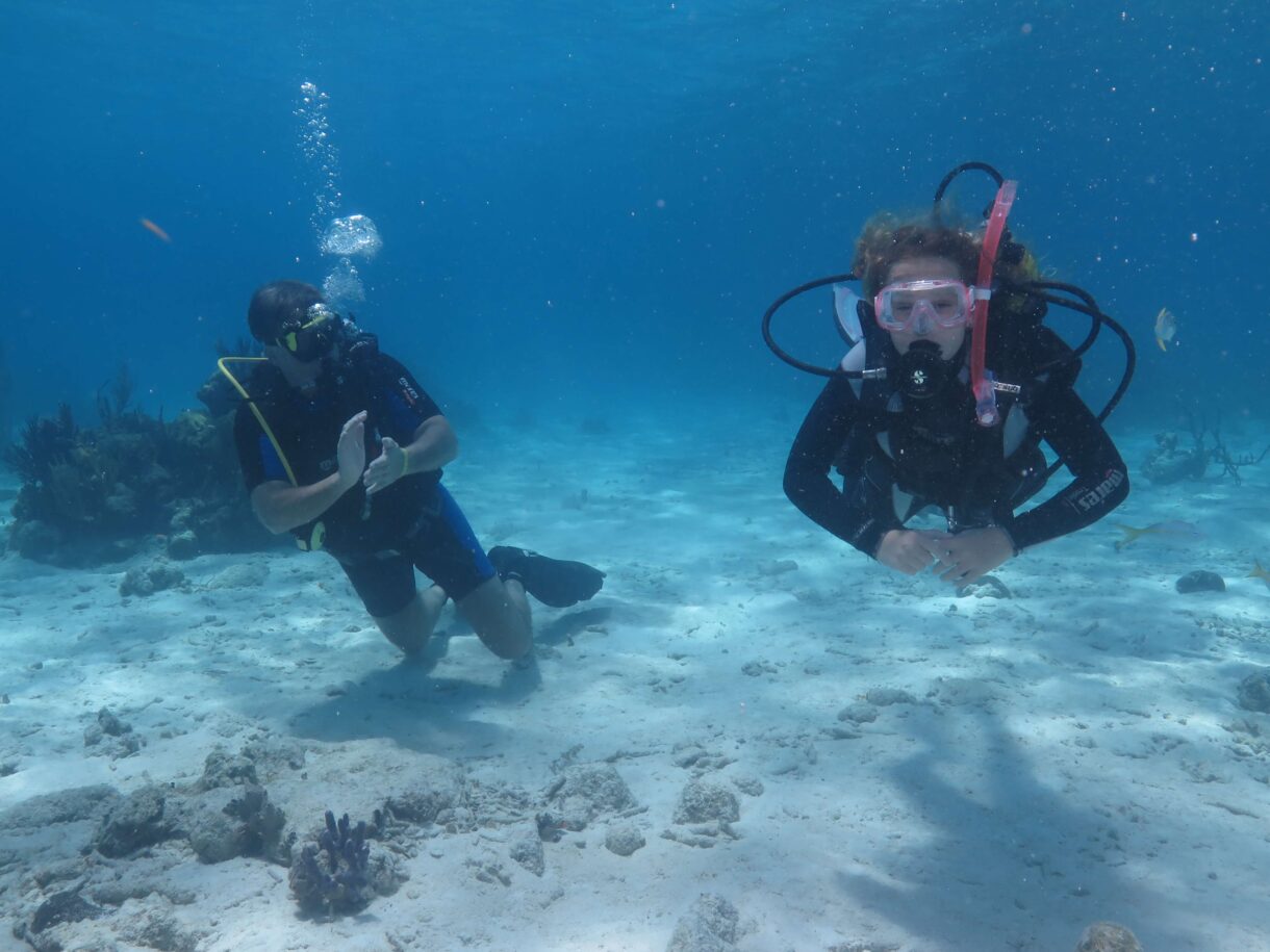 Underwater scuba diving scene at Coral Beach Varadero, showing a beginner diver and instructor exploring vibrant coral reefs with tropical fish.